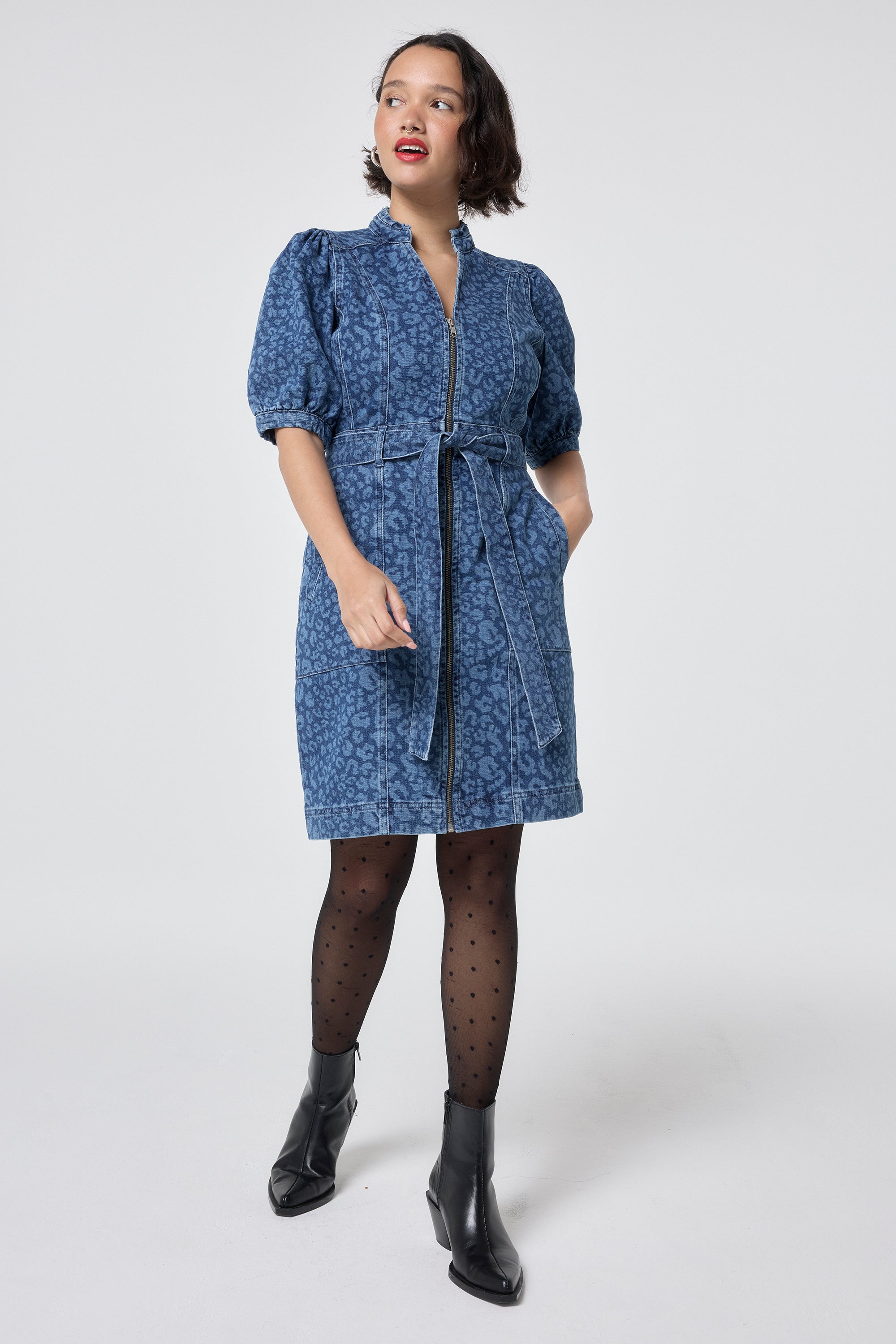 Scamp and Dude Authentic Indigo Leopard Zip Detail Short Denim Dress | Model wearing a denim leopard print short dress with a tie waist detail, paired with tights and black boots.