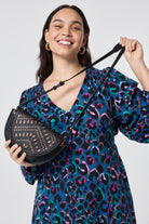 Scamp and Dude Black with Gold Laser Cut Saddle Bag | Model wearing a teal dress with rainbow leopard print paired with a black saddle bag that features laser cut detail.