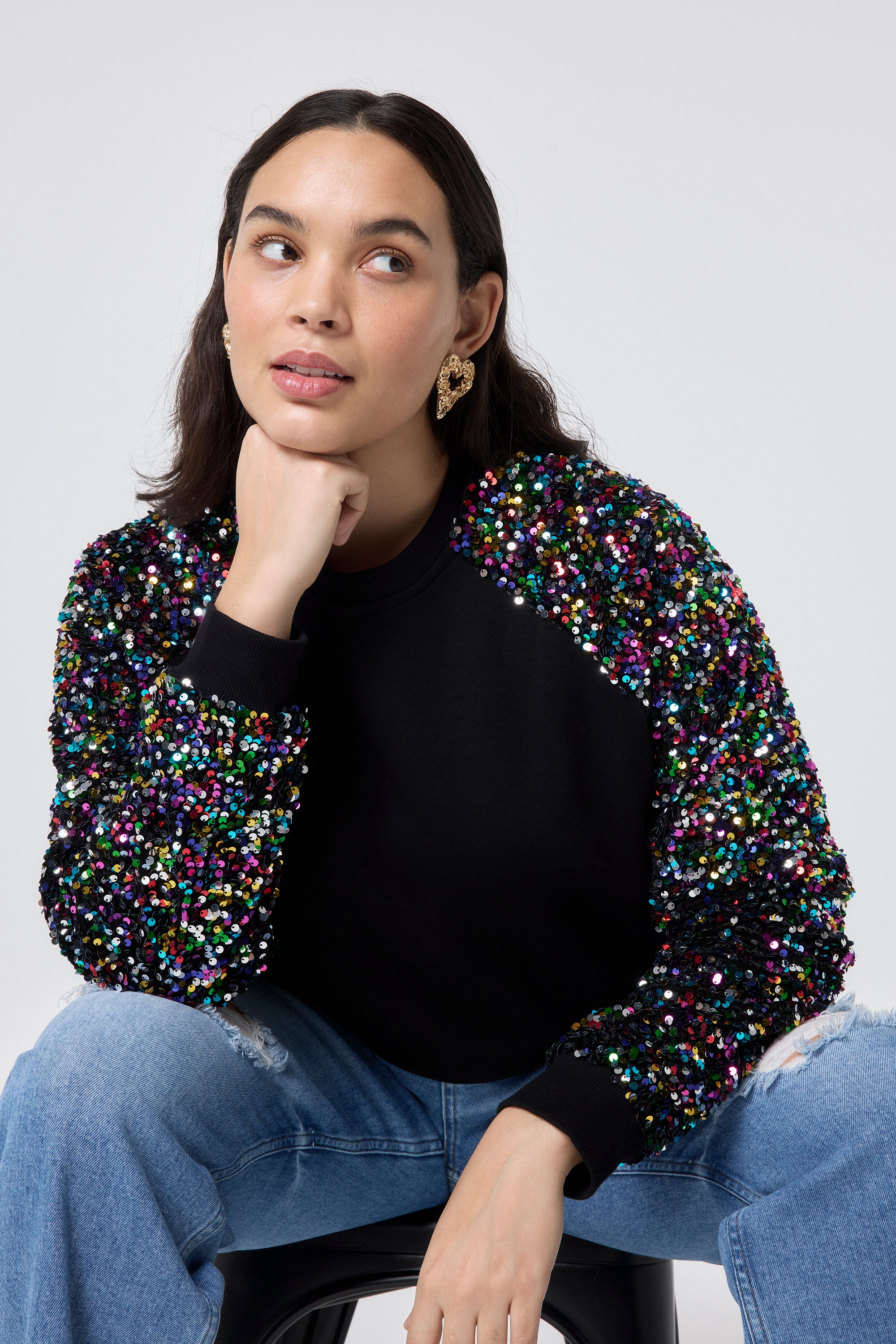 Scamp and Dude Black with Rainbow Sequin Sleeve Raglan Sweatshirt | Model wearing a black sweatshirt that has rainbow sequin sleeves paired with blue distressed jeans.