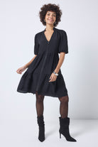 Scamp and Dude Black Textured Zip Detail Tiered Short Dress | Model wearing a short black textured dress with a zip front detail, worn with black polka dot tights and boots.