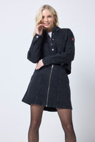 Scamp and Dude Black Heat Seal Zip Front Denim Mini Skirt | Model wearing a black denim mini skirt with a matching shacket featuring heat seal detail. Worn with black tights and boots.