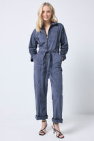 Scamp and Dude Ink Blue Tie Front Boiler Jumpsuit | Model wearing a ink blue jumpsuit featuring a zip front and tie waist, paired with black strappy heels.