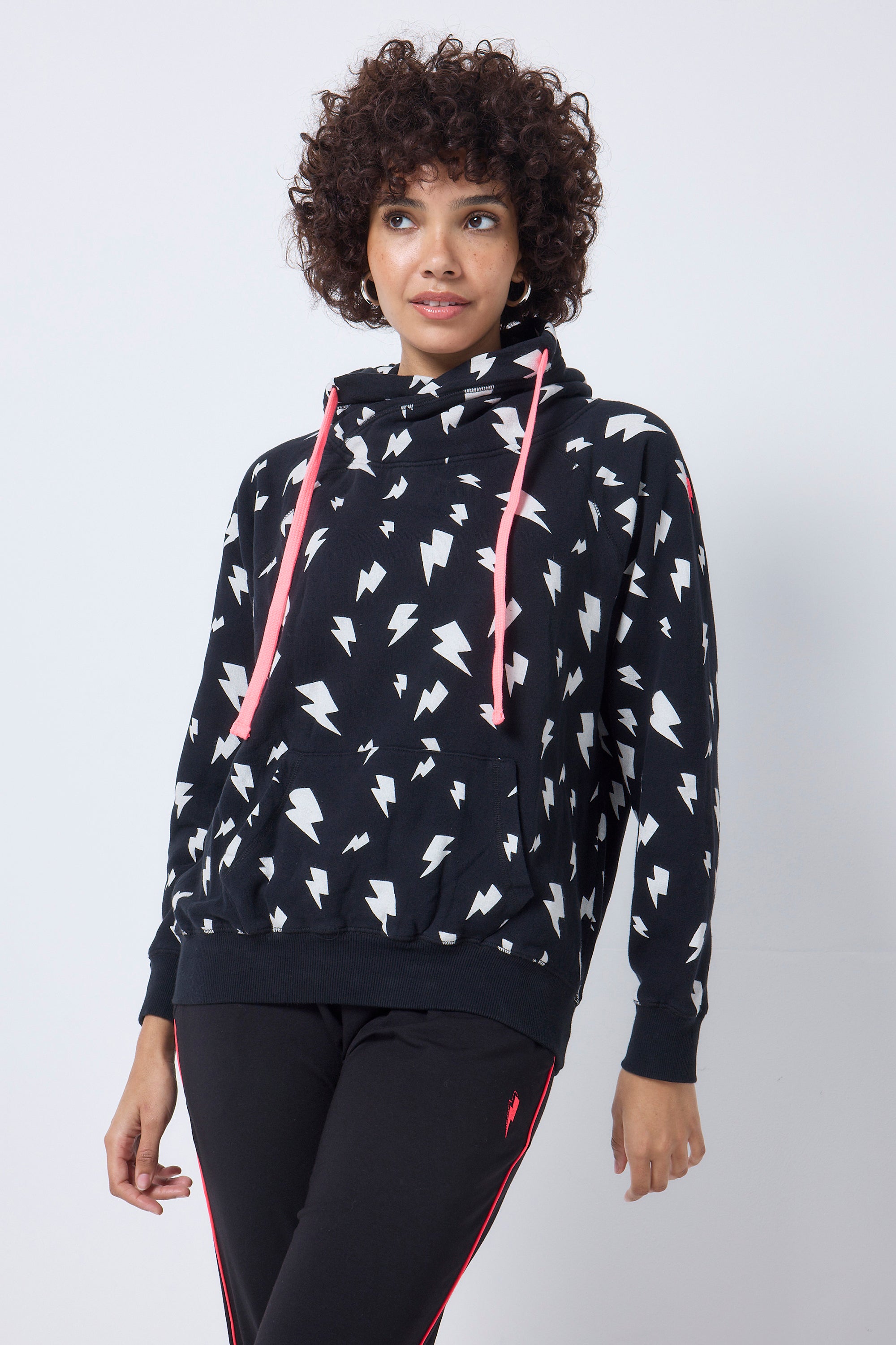 Scamp and Dude Black with White Lightning Bolt Cowl Neck Hoodie | Model wearing a black hoodie with a white lightning bolt print and coral drawstrings, paired with black joggers.