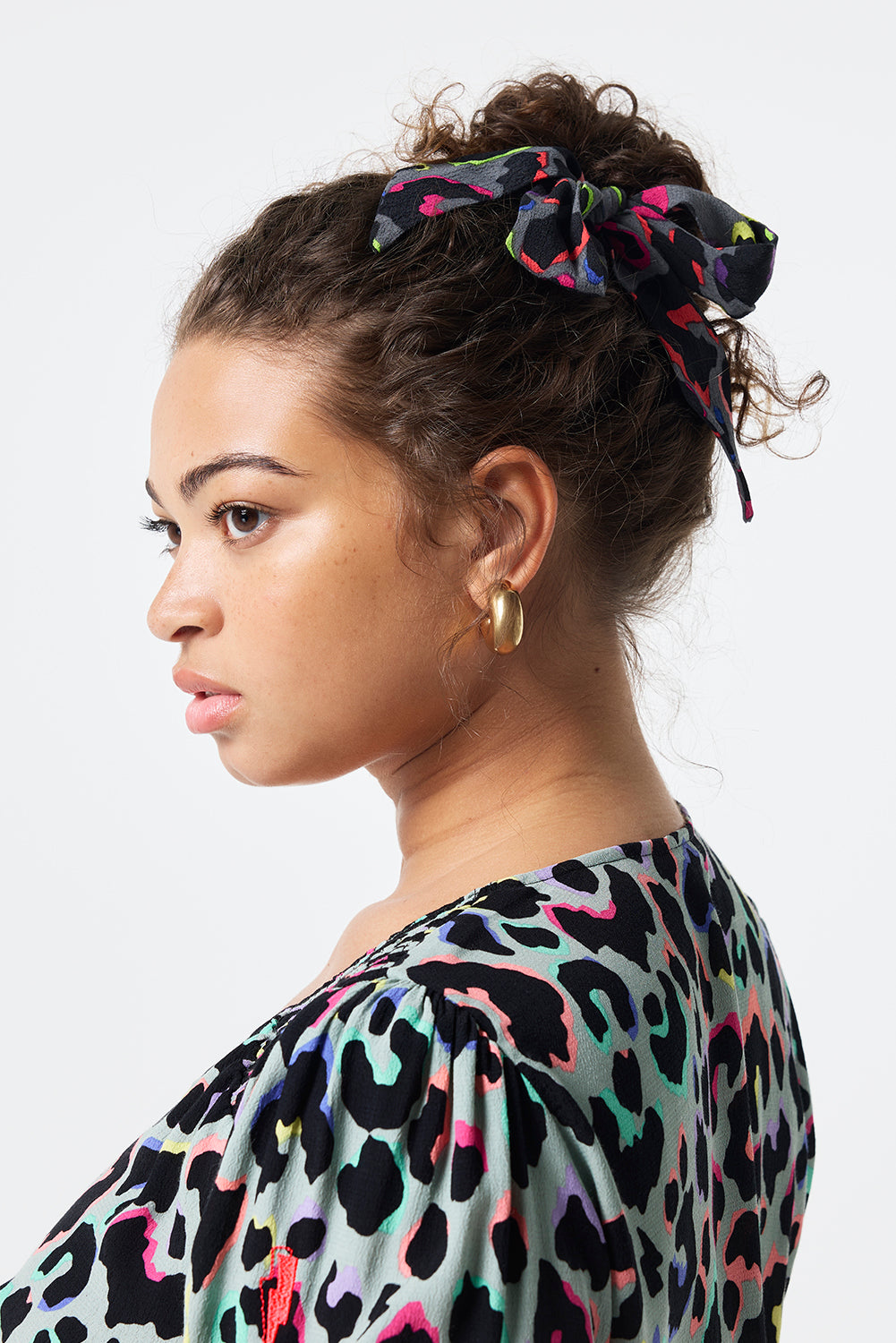 Scamp and Dude Grey with Rainbow Shadow Leopard Bow Scrunchie | Model wearing her hair in a bun with a grey scrunchie featuring rainbow shadow leopard print.