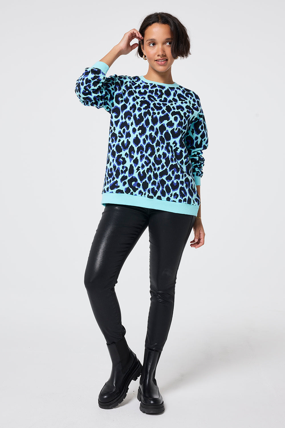 Scamp and Dude Turquoise with Black and Blue Shadow Leopard Oversized Sweatshirt | Model wearing an oversized crew neck sweatshirt with blue and black leopard print paired with a pair of black coated jeans and chunky boots.