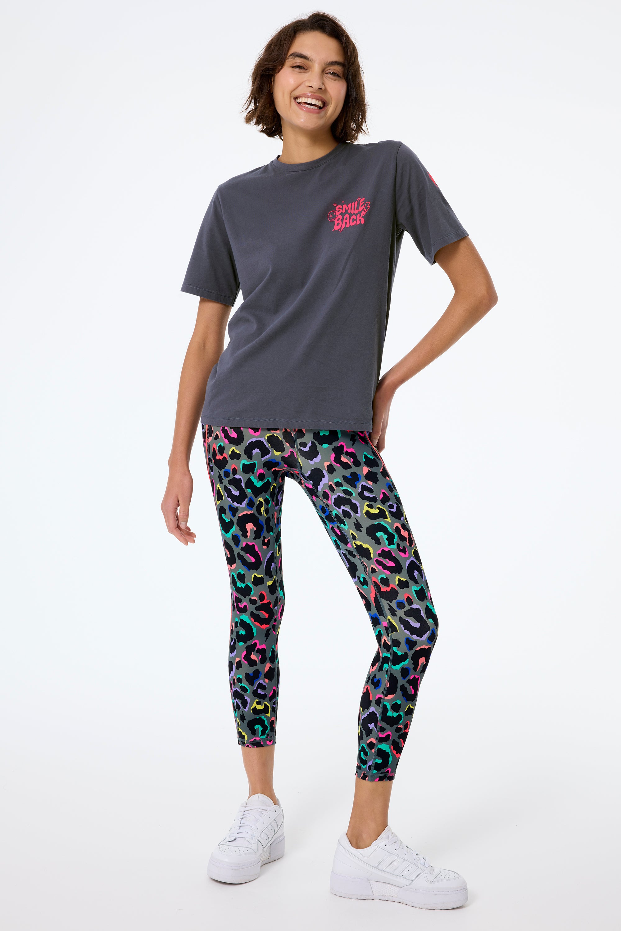 Scamp and Dude Dark Khaki with Rainbow Shadow Leopard 7/8 Length Active Leggings | Model wearing a grey t shirt with neon details paired with a pair of khaki 7/8 leggings with rainbow leopard print and white chunky trainers.