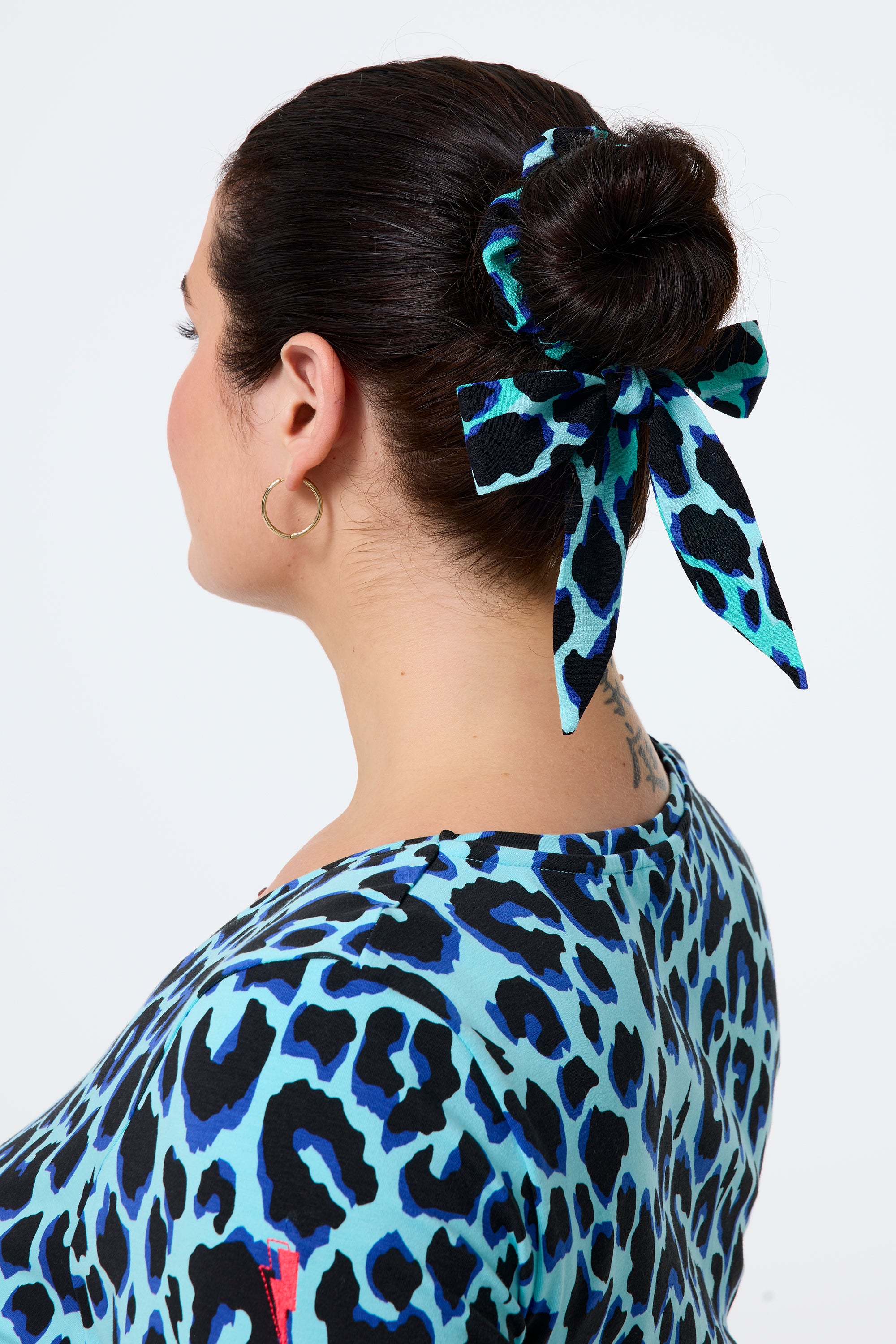 Scamp and Dude Turquoise with Black and Blue Shadow Leopard Bow Scrunchie | Model wearing a turquoise t shirt with a matching scrunchie in her hair.