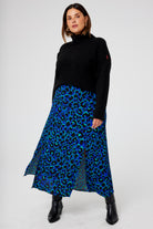 Scamp and Dude Blue with Green and Black Shadow Leopard Split Front Skirt | Model wearing a black turtle neck jumper with a blue midi skirt which features green and black shadow leopard print.