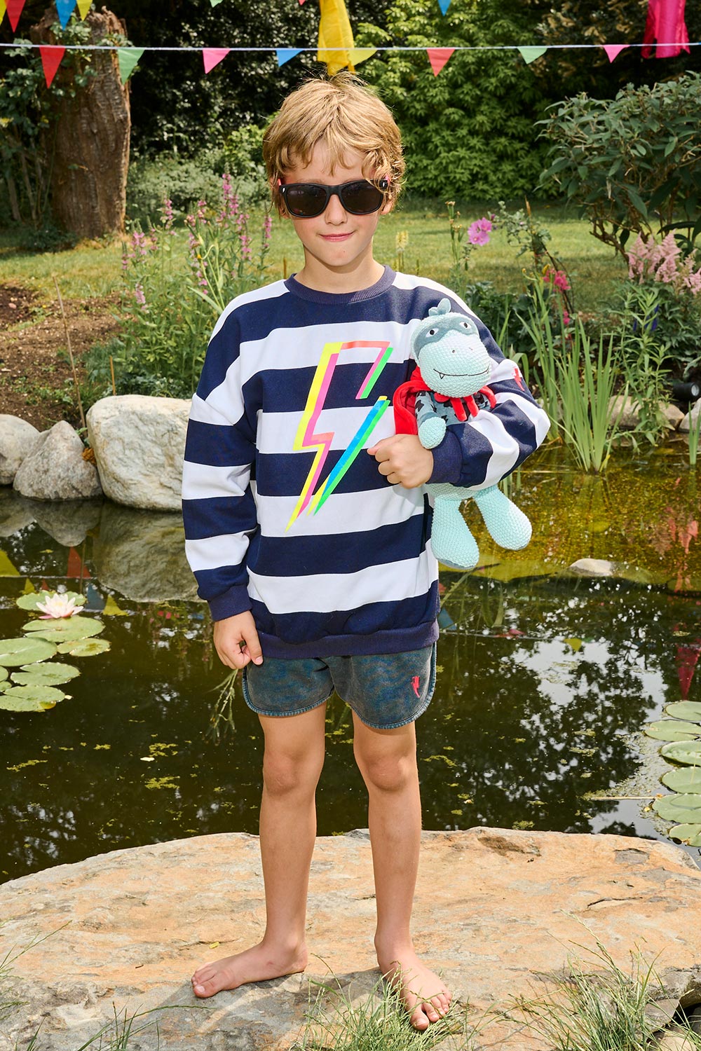 A boy wearing a navy with white stripe oversized sweatshirt with a multi-coloured neon lightning bolt on the front